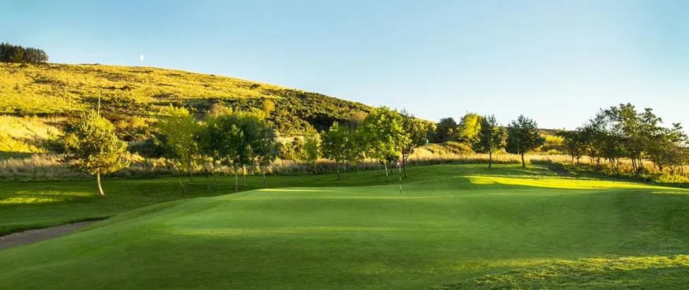 A sunlit green below the hill